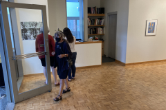 Image from the opening reception, prints are hanging on the walls and a small group of visitors is gathered in various spots around the work.
