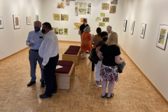 Image from the opening reception, prints are hanging on the walls and a small group of visitors is gathered in various spots around the work.