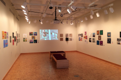 Installation shot of For The Record, including the majority of the gallery, including the projected videos on the rear wall.
