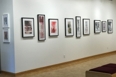 Photograph of Ira Epsteins work installed in the gallery. This image shows the galleries left wall, and 11 framed pieces are hung down the wall. All the works are modified book pages and contain colorful ink on them.