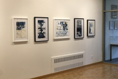 Photograph of Ira Epsteins work installed in the gallery. This image shows part of the galleries right wall, and 5 framed pieces are hung down the wall. All the works are modified book pages and contain colorful ink on them.