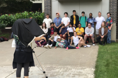 Image from Jenn Libby's Wet Collodion Demonstration. This image shows Jenn behind a camera, which is pointing at a group of students posing for the photograph.
