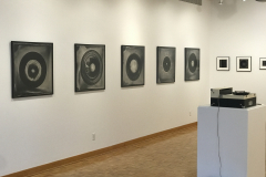 Installation image of Jenn Libby exhibition Echoes from the Ether.  This image shows a detail of the left wall containing large black and white abstract images. A small area of the back wall can be seen, showing smaller black and white abstract images. In the foreground is an old record player.