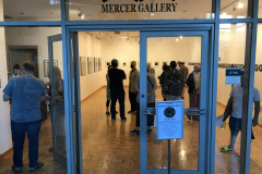 Image from the opening reception of Jenn Libby's exhibition Echoes from the Ether. This image is from outside the gallery, looking into the gallery showing a group of people inside.