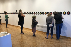 Image from the opening reception of Jenn Libby's exhibition Echoes from the Ether. This image shows people lined up in front of the long row of seven inch records, looking at the imagery in the center.