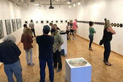 Image from the opening reception for Jenn Libby's exhibition Echoes from the Ether. This image shows a group of people standing near some photographs, talking.