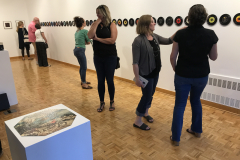 Image from the opening reception of Jenn Libby's exhibition Echoes from the Ether. This image shows people lined up in front of the long row of seven inch records, looking at the imagery in the center.