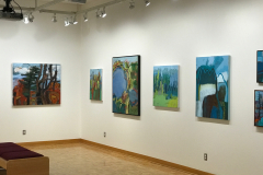 Installation shot of Judy Gohringers Mercer Gallery exhibition. This image shows the back right corner of the gallery. On the rear wall we see one large colorful landscape painting, and on the right wall we see six more colorful landscape paintings, in varying sizes.