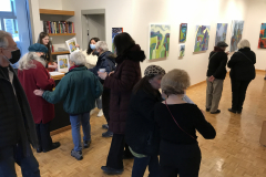 Photograph from the opening reception for Judy Gohringer. This image shows a group of people standing around the desk looking at the catalog for the exhibition.