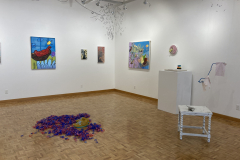 A wider shot of the rear right wall, showing a variety of colorful paintings, two sculptures, and some painting done on the wall.