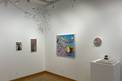 The rear right corner of the gallery, showing a variety of colorful paintings, and a small sculpture on a pedestal.