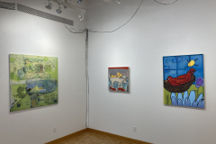 The rear left corner of the gallery, showing a variety of colorful paintings,.