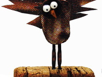 A mixed media sculpture of a crazy looking bird standing on a wooden plank.