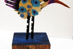 A mixed media sculpture of a crazy looking bird standing on a wooden plank.