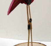 A mixed media sculpture of a crazy looking bird standing on a wooden plank.