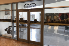 Installation shot of glass entry doors to gallery. Down the center of all the glass are images of a landscape, matching the horizon line beyond the space.