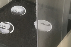 Installation shot of a pedestal, with soil and three ceramic ovals containing war imagery.