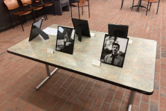 A close up image of one of the tables, containing five frames propped up, and in the two facing us we can see portraits of people.