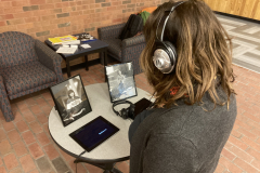 An over the shoulder photograph, showing a woman listening to the audio interviews and looking at the framed portrait on the table.