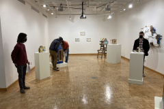 A wide photograph of the gallery showcasing Nate Hodge's sculptures. Among the work are various guests looking at the art and talking with one another.