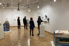 A wide photograph of the gallery showcasing Nate Hodge's sculptures. Among the work are various guests looking at the art and talking with one another.
