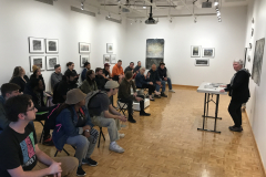 Image of Pat Bacon lecturing in the gallery with a number of people watching.