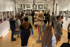 Photograph from the artist reception for Patti Russotti. Large groups of people talk in the gallery while others look at the art on the walls..