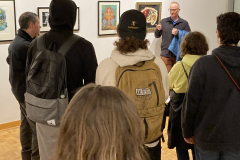 An image from the opening reception, in which many people listen to an artist speaking.