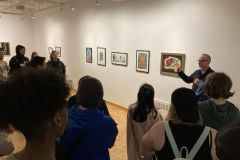 An image from the opening reception, in which many people listen to an artist speaking.