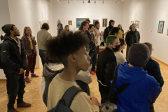 An image from the opening reception, in which many people listen to an artist speaking.