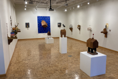 Detail image of the Robert Booth gallery installation, showing an overview of the gallery. In th eimage we can see the left wall with five sculptures hanging, the rear wall with three sculptures hanging, the right wall with four sculptures hanging, and three floor sculptures on low pedestals down the center of the room.