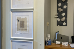 Detail image of the Robert Booth gallery installation, showing three drawings hanging vertically, and one sculpture that is hanging behind the desk in the photograph.