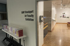 An image of the installation for the SUNY Brockport exhibition. This image shows the exterior of the gallery, and a piece outside and a sculpture inside the gallery.